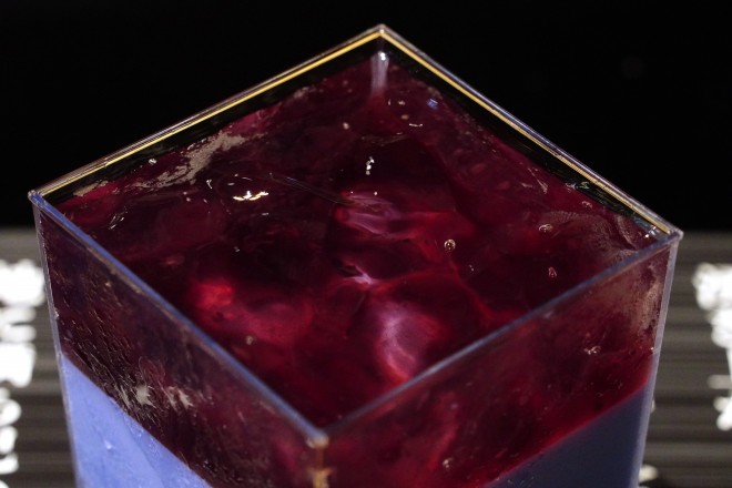The “Hadō No. 90: Kurohitsugi Pudding” served at BLEACH WORLD features a dark purple milk pudding layered with blueberry sauce and clear jelly—presented atop a printed incantation sheet